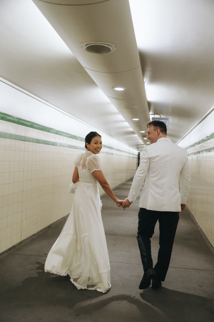 Jamie and Lilly walking hand in hand through a tiled tunnel in wedding attire